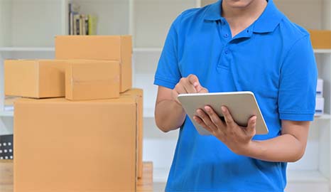 Delevery person holding tablet with piled up carboard boxes behind