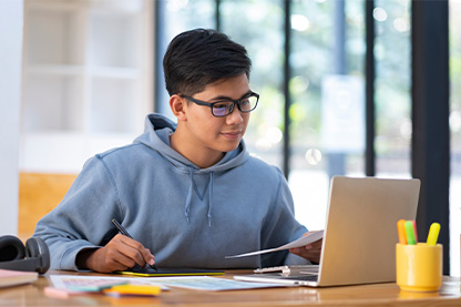 Person at desk with laptop holding and looking at sheet of paper