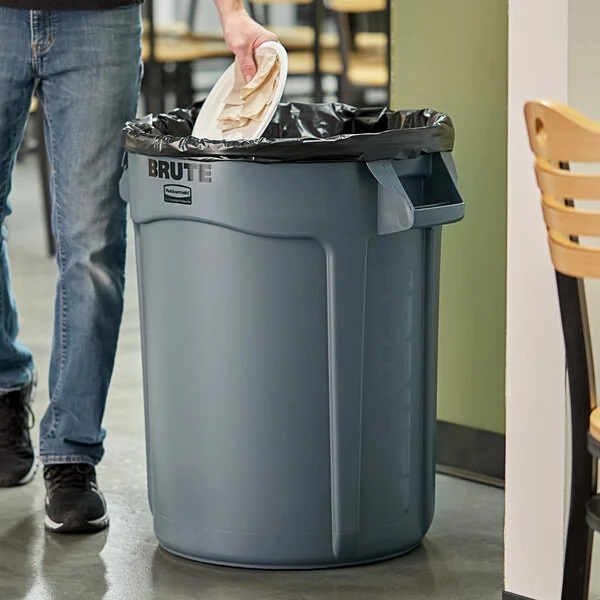 a man throughs garbage in the rubbermaid Brut garbage can
