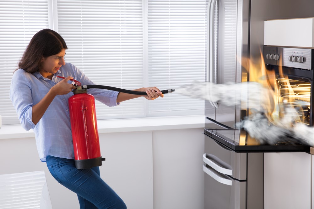 a woman puts out a kitchen fire with a fire extinguisher