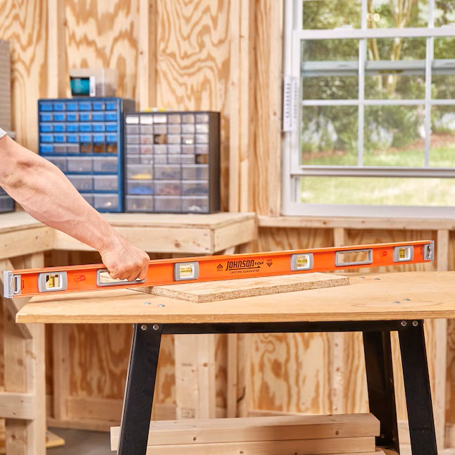 an arm reaches for a Johnson Aluminum I-Beam Level on a workbench