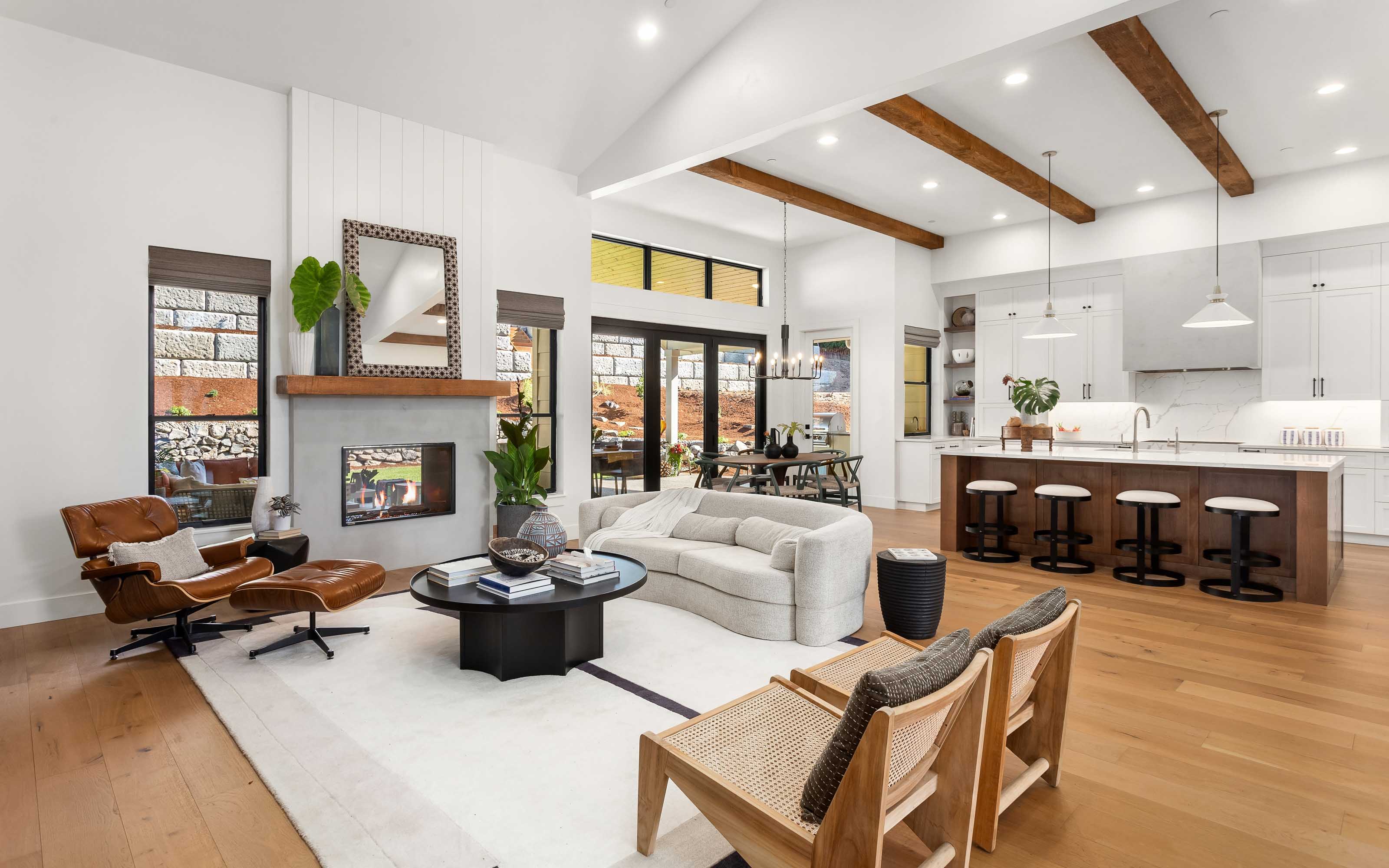 Elegant Modern Interior with Natural Accents Open-concept living room and kitchen with mid-century modern furniture, white cabinetry, exposed wooden beams, and large glass doors overlooking autumn foliage.