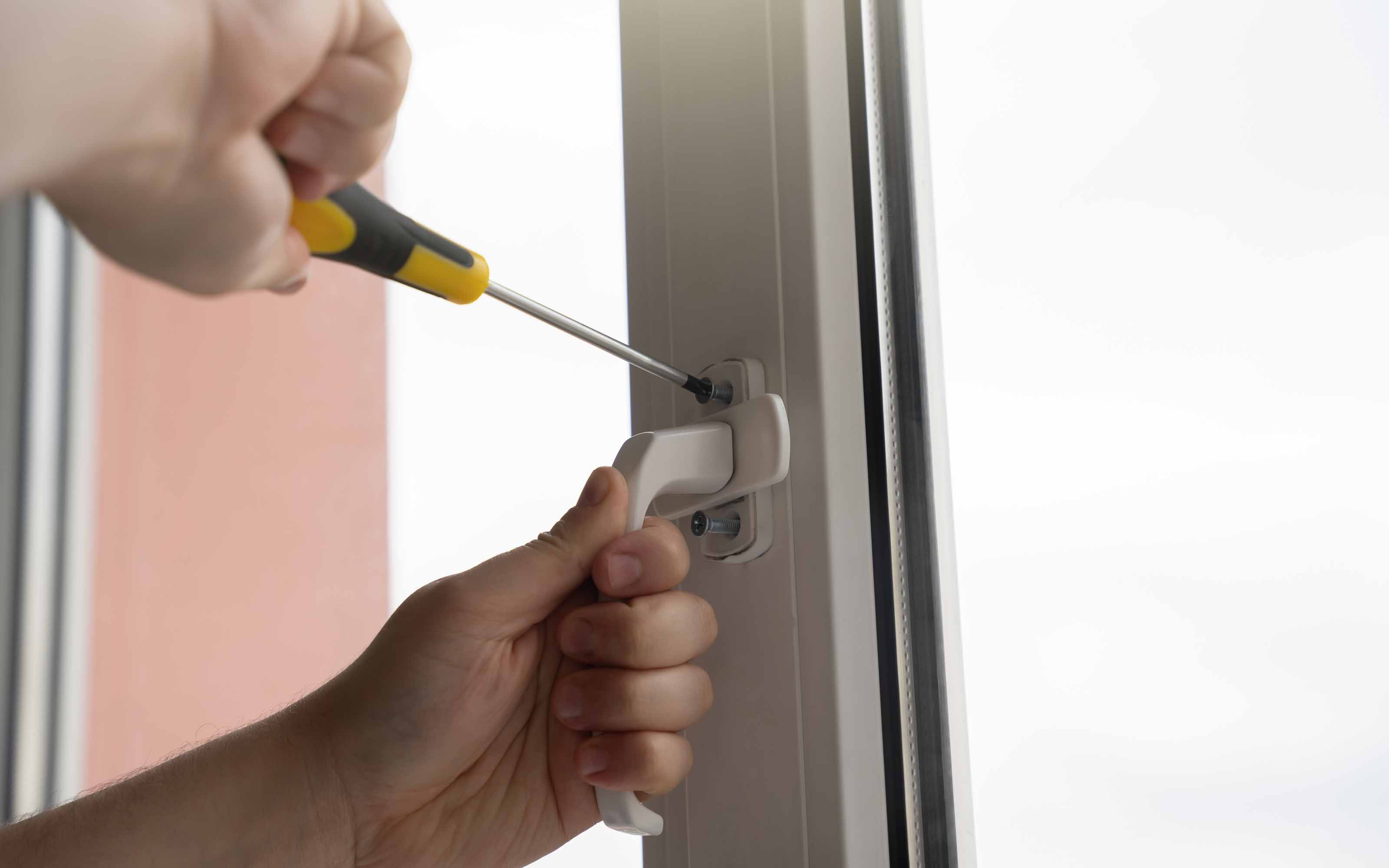 Person using a screwdriver to repair or tighten a window handle on a modern energy-efficient window.