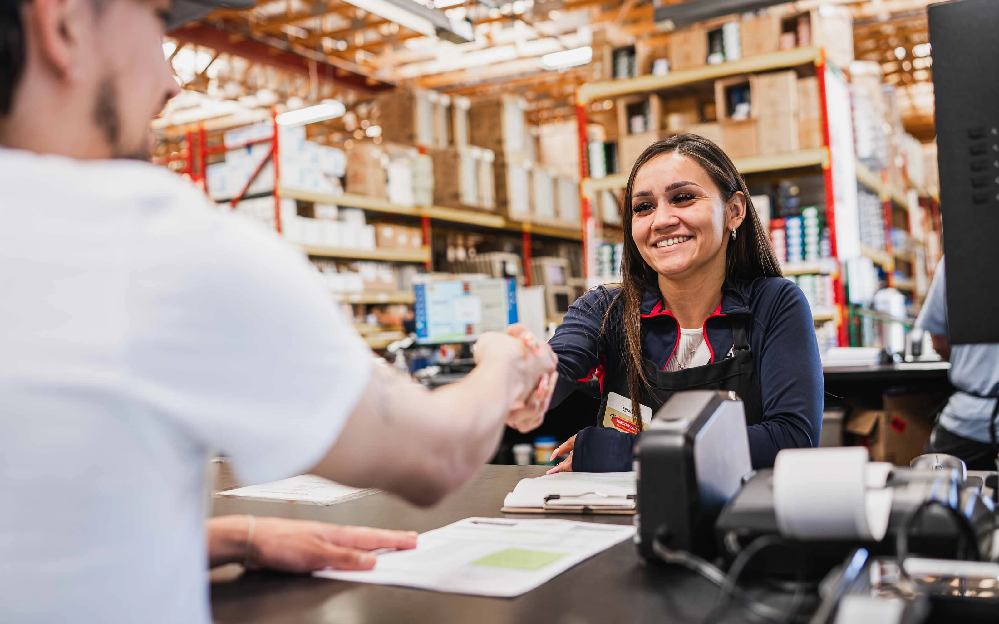 Contractor and customer shaking hands at a home improvement store counter while discussing building materials