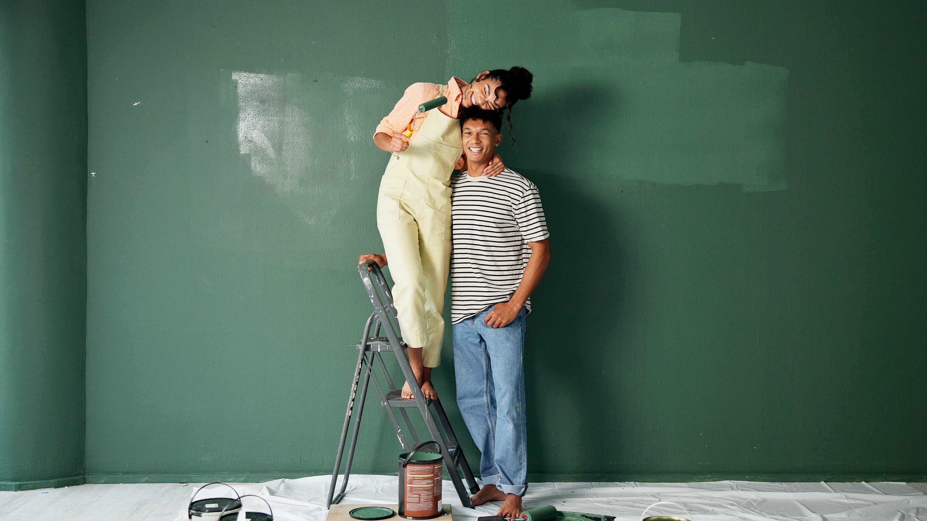 A Couple Painting the Room Happy couple painting a wall green during a budget-friendly home renovation project.
