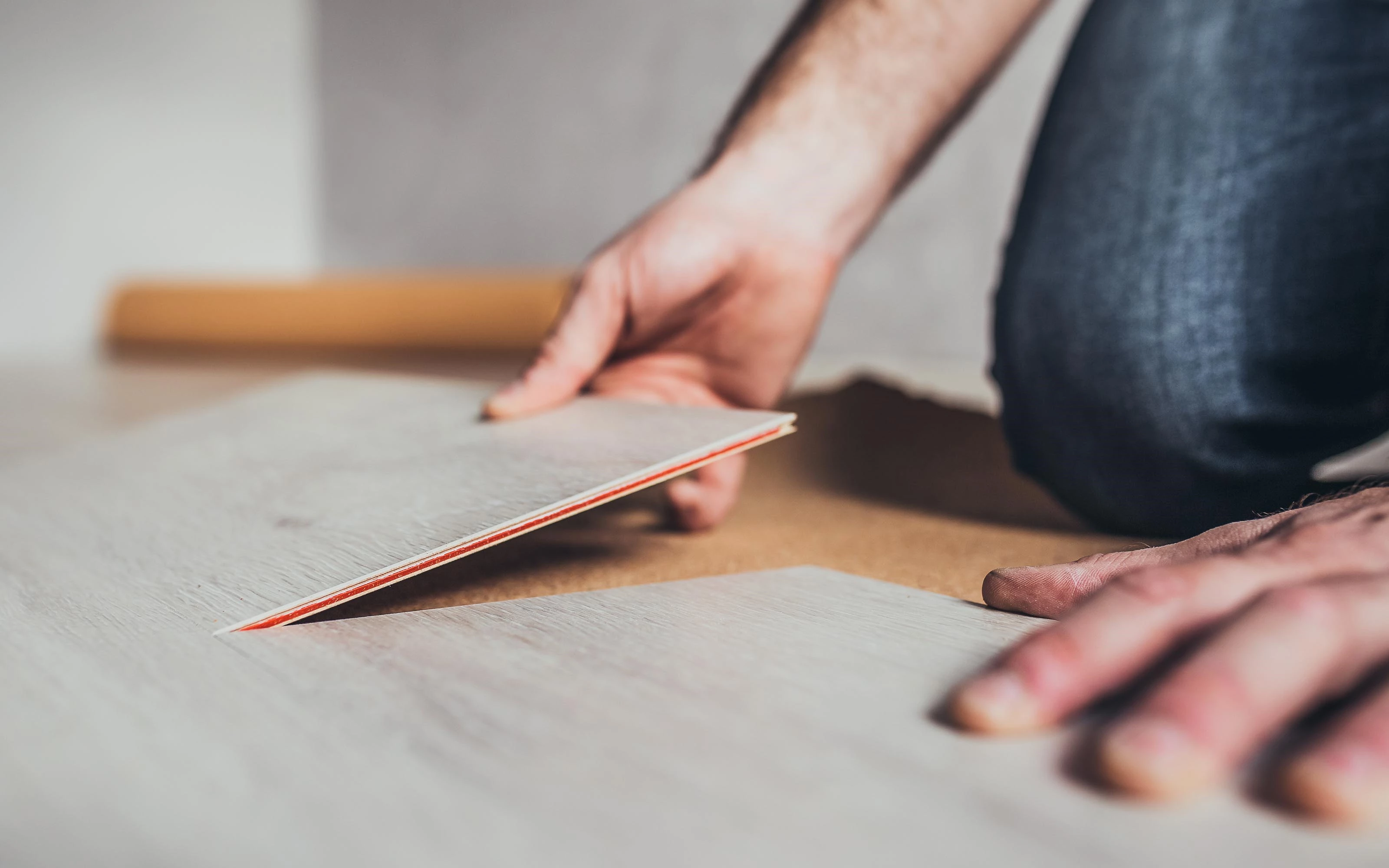 Close-up of a person installing vinyl flooring, showing hands carefully aligning and placing the vinyl tiles.