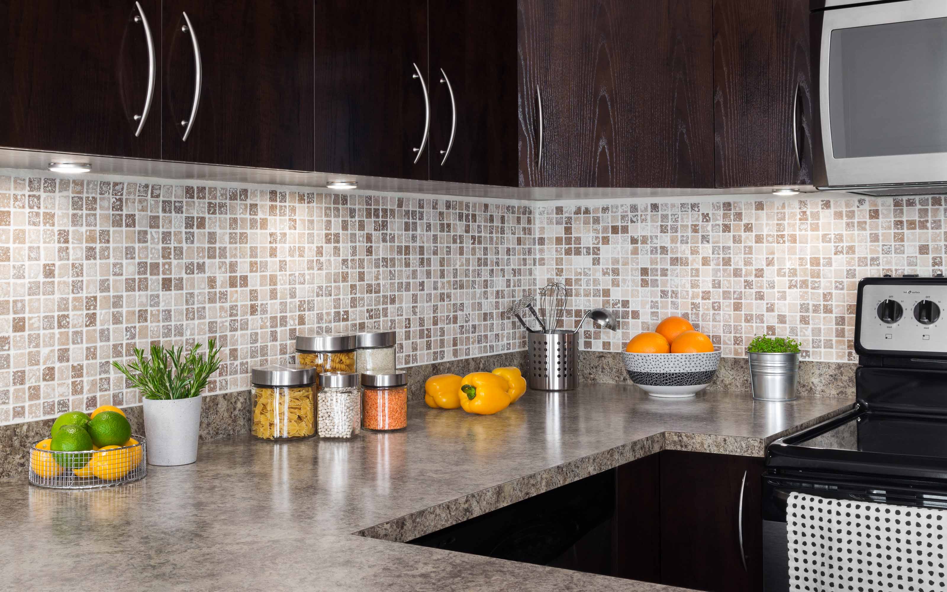 Modern kitchen countertop with dark cabinets, mosaic tile backsplash, and stainless steel appliances