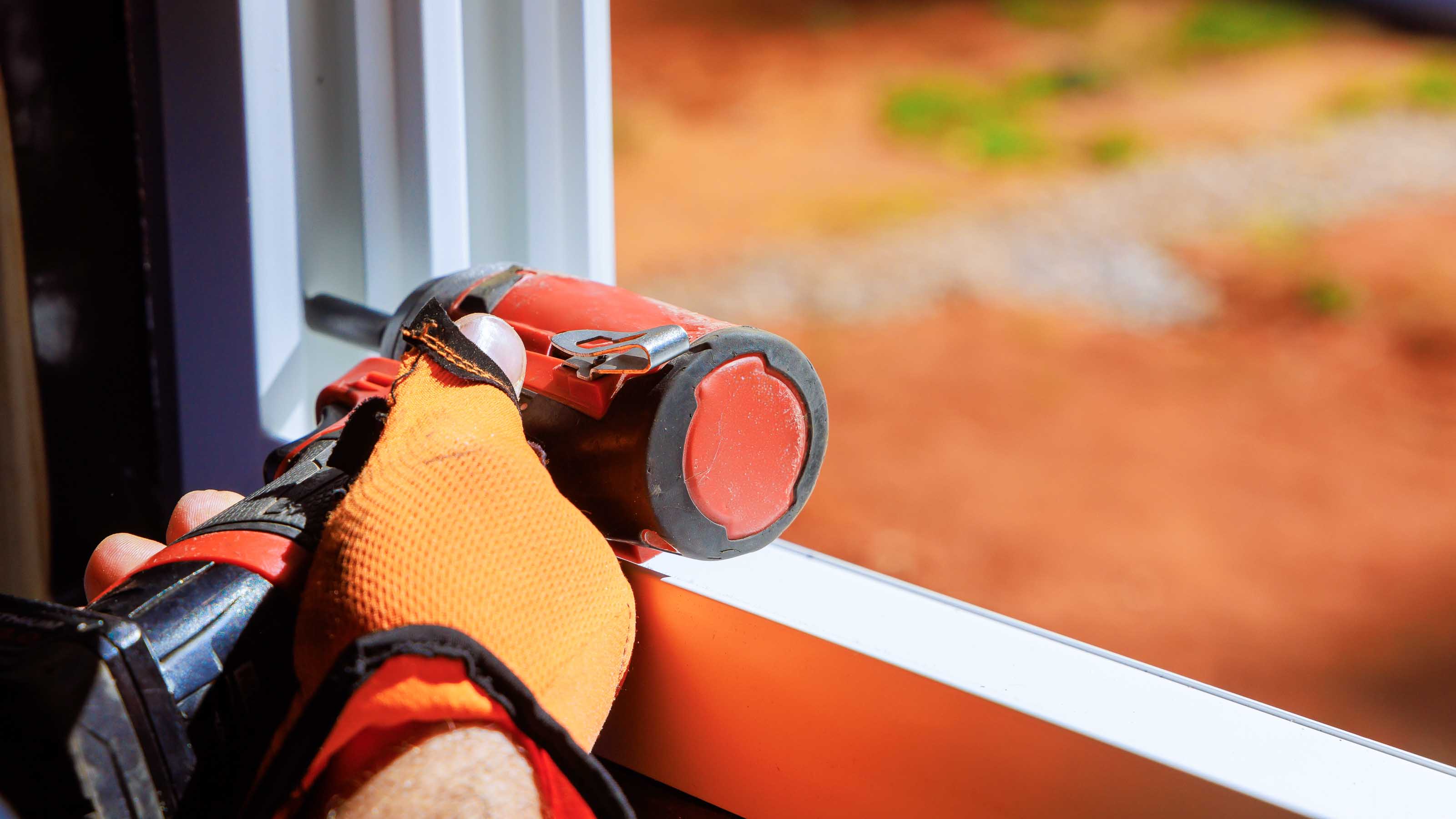 Worker in protective gloves installing energy-efficient window frame with a power tool.