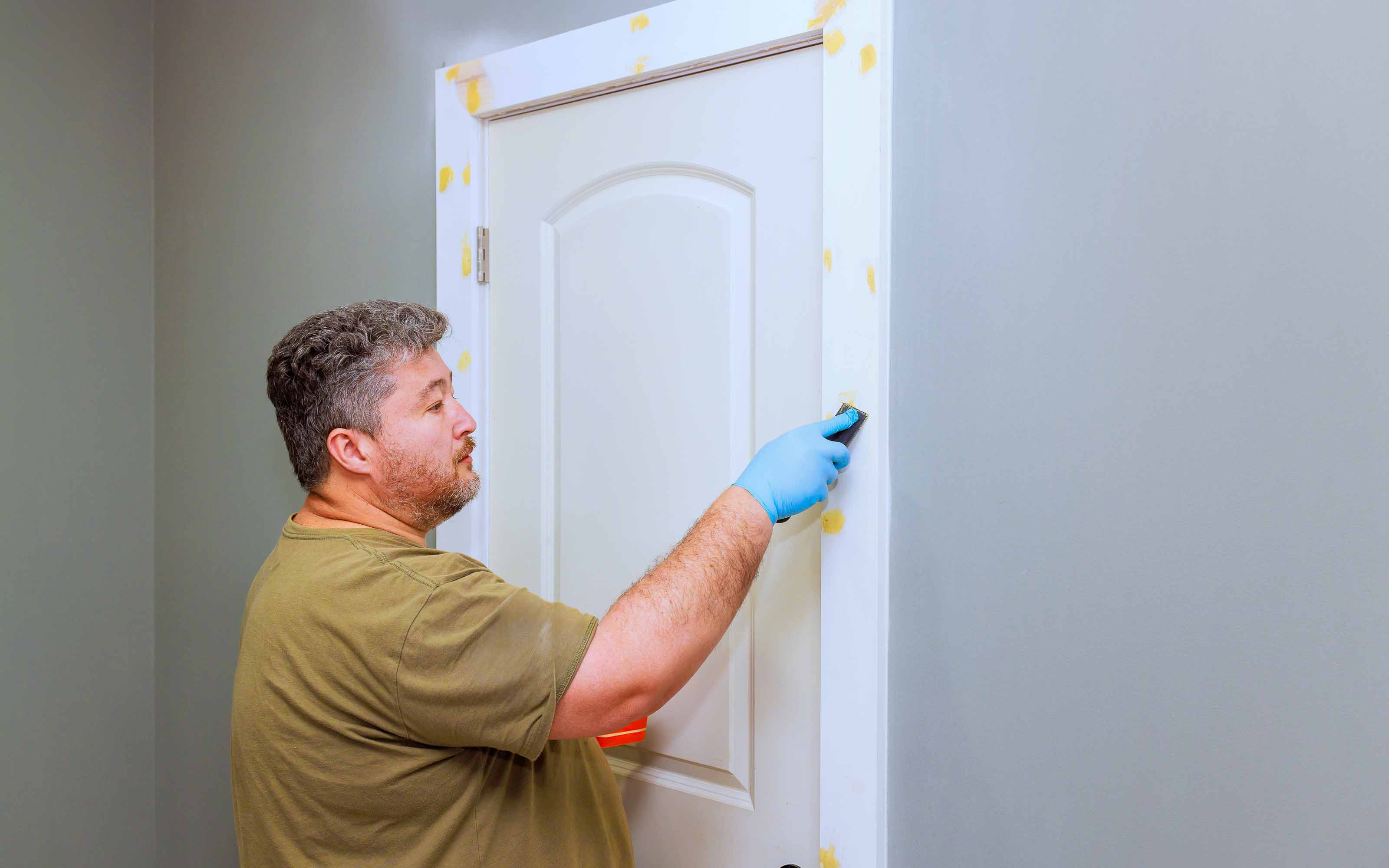 Man sanding and preparing door frame for painting in a home interior