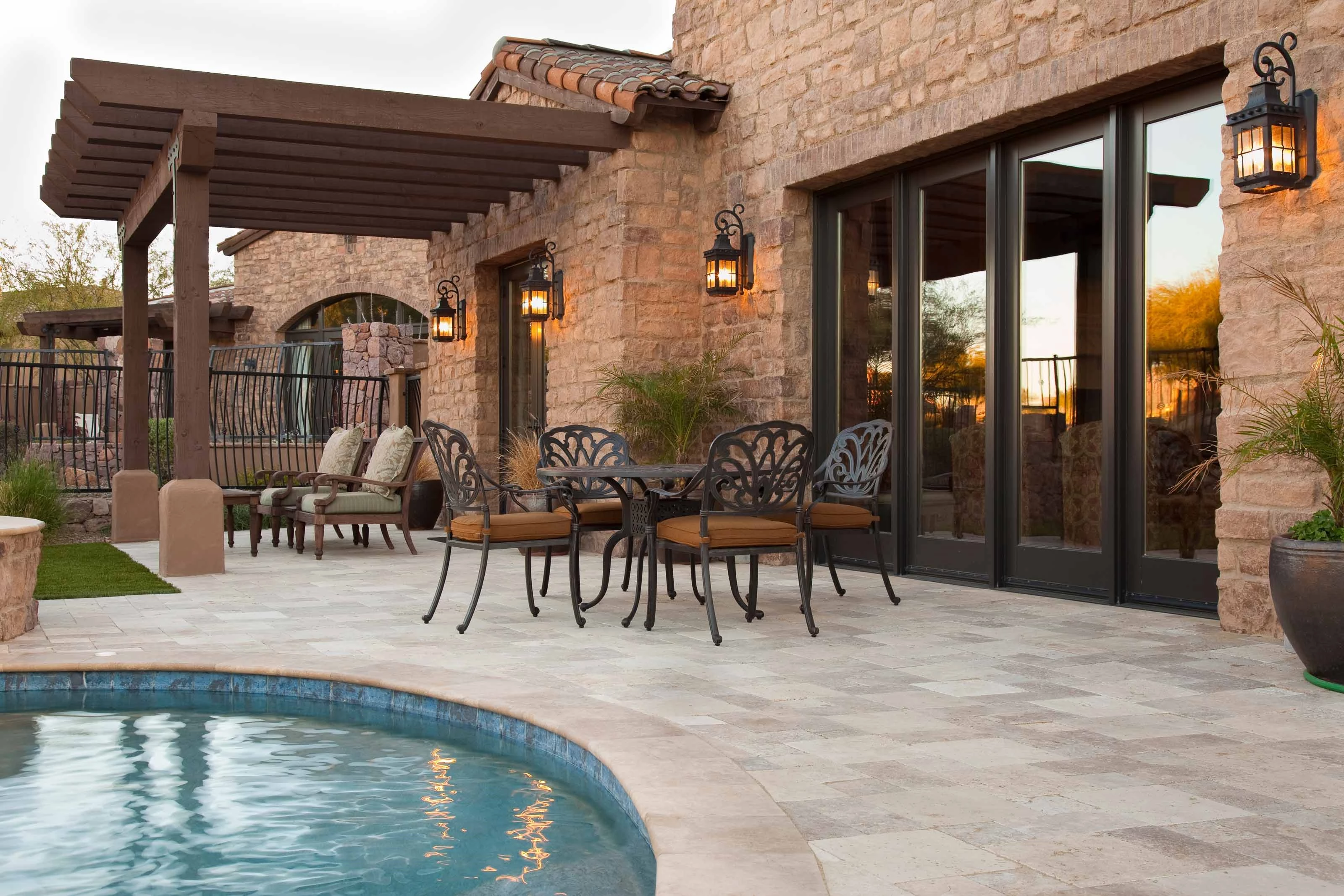 Elegant Outdoor Patio with Pergola and Pool A luxurious outdoor patio area with a stone facade, featuring a pergola, wrought iron furniture, and a swimming pool