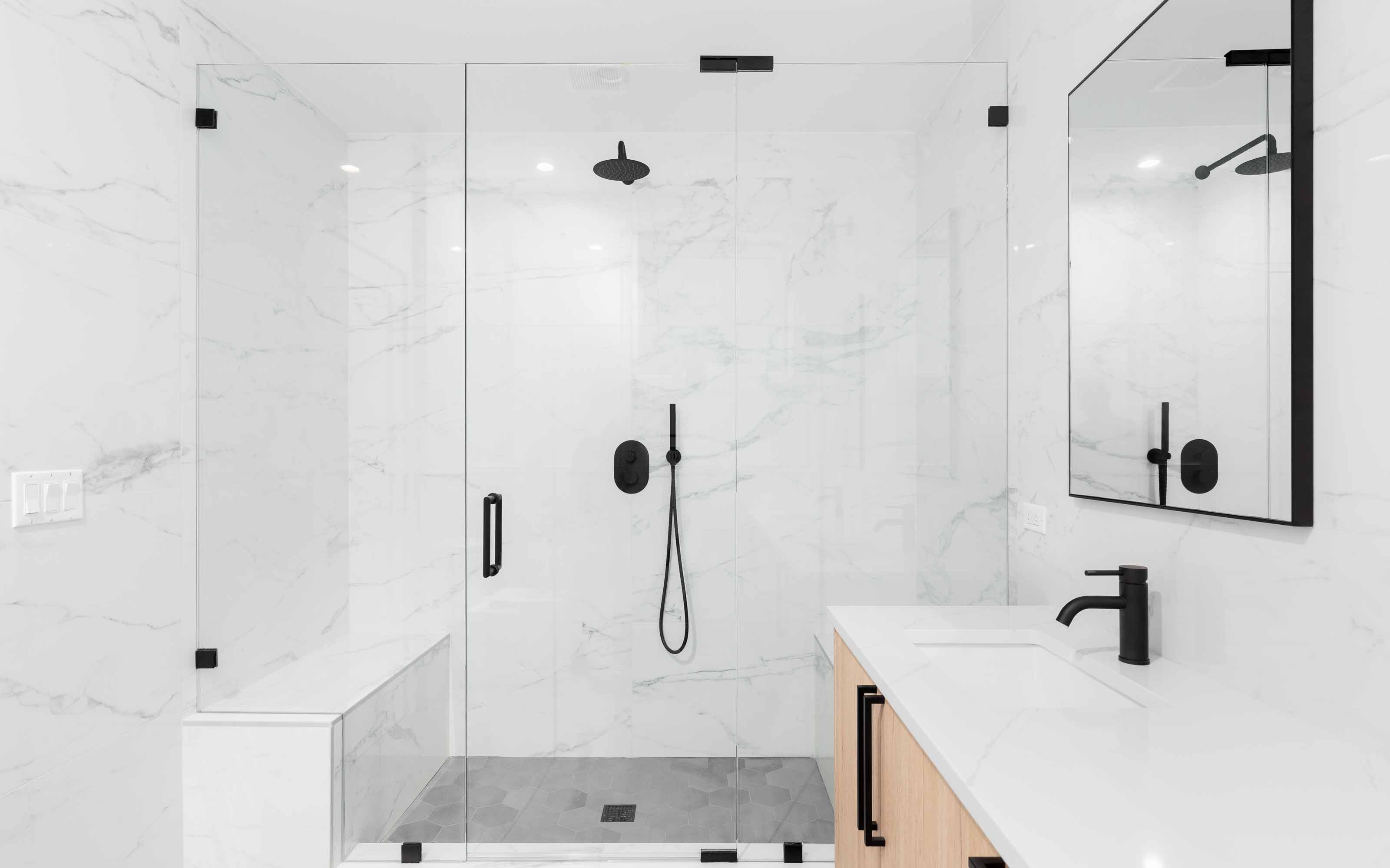 Modern frameless glass shower door with black hardware in a white bathroom